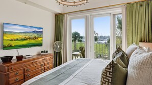 A bedroom with a large bed, a television, a dresser, and a balcony with a view. - Great Condo with views of the Marina, Frederica River & the St Simons Sound (St Simons Island)