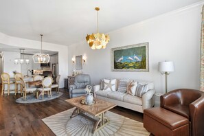 Ein modernes Wohnzimmer mit Essbereich, einem grauen Sofa, einem braunen Ledersessel, einem Holztisch und einer Kristallleuchtre.
