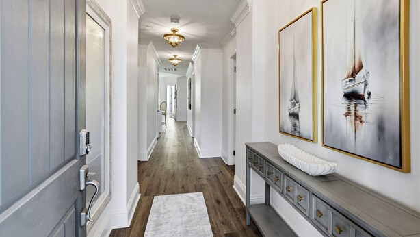 A hallway with a white console table, a white bench, and a large framed painting of a sailboat. - Great Condo with views of the Marina, Frederica River & the St Simons Sound (St Simons Island)