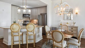 A modern kitchen with a central island, stainless steel appliances, and a dining area with wooden chairs and a table. - Great Condo with views of the Marina, Frederica River & the St Simons Sound (St Simons Island)