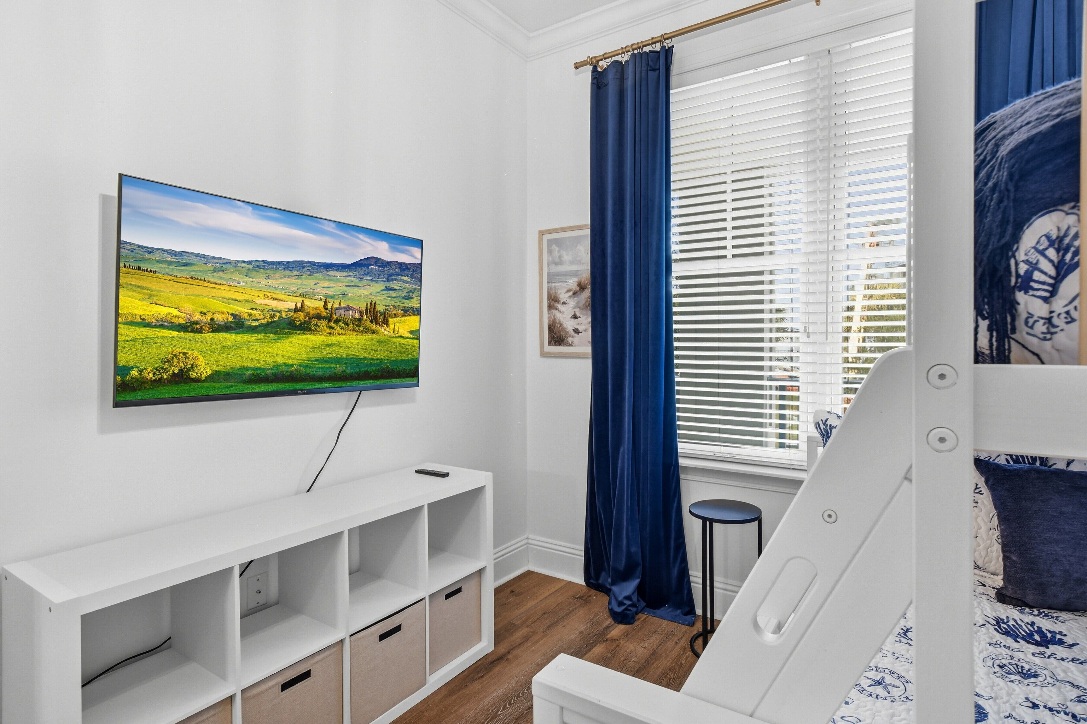A bedroom with a bed, a TV mounted on the wall, a window with curtains, and a bedside table.