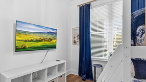 A bedroom with a bed, a TV mounted on the wall, a window with curtains, and a bedside table. - Great Condo with views of the Marina, Frederica River & the St Simons Sound (St Simons Island)