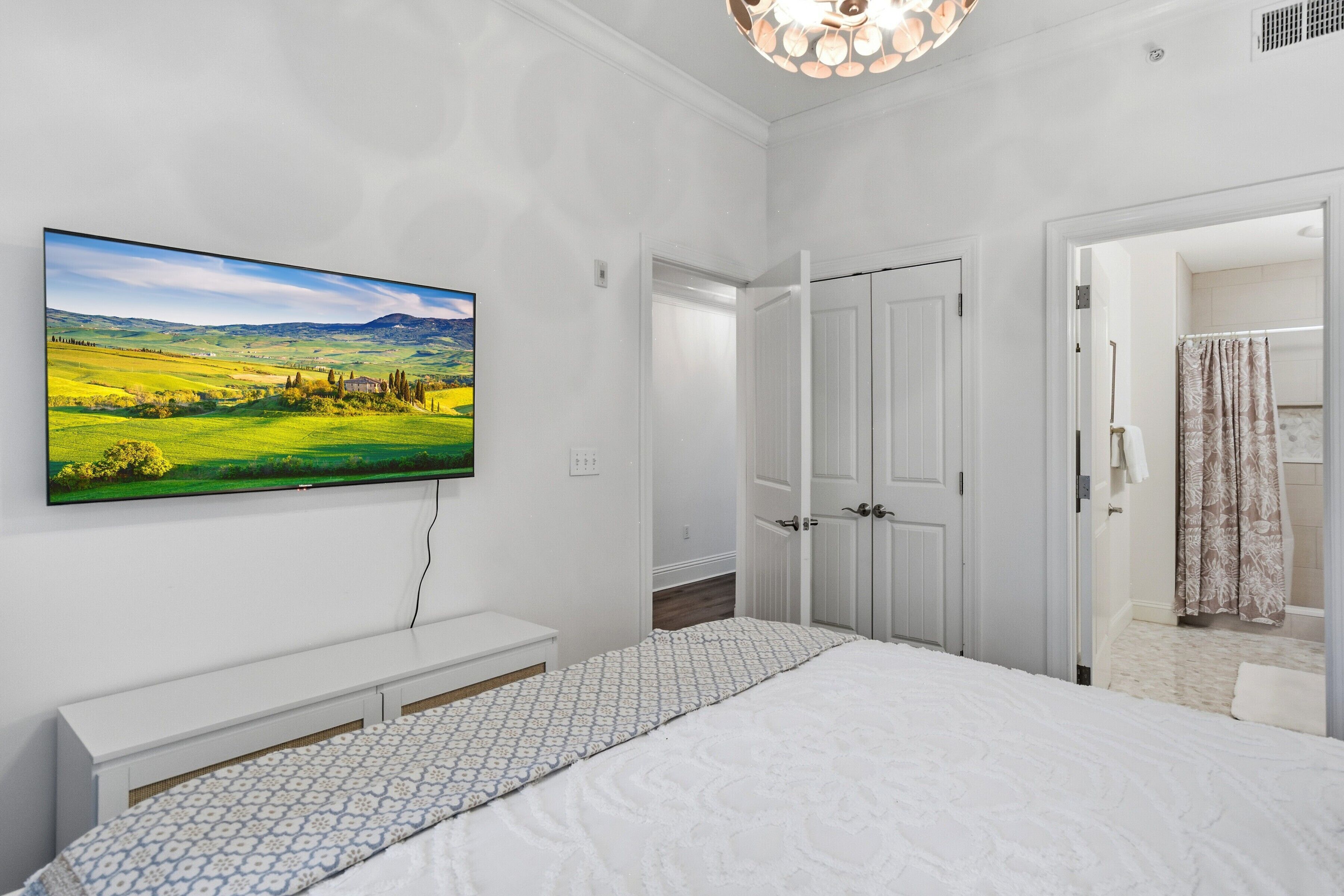 Une chambre à coucher avec un lit, un téléviseur fixé au mur et une porte donnant sur une salle de bain.