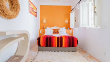 A bedroom with a bed, a white chair, a rug, and a wall with a painting.