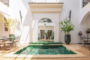 Un patio con piscina, zona de estar y plantas en macetas.