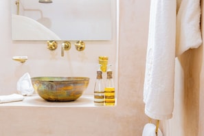 A bathroom with a large bowl sink, two bottles with labels, a towel, and a mirror above the sink. - Riad Thaïs (Marrakech)