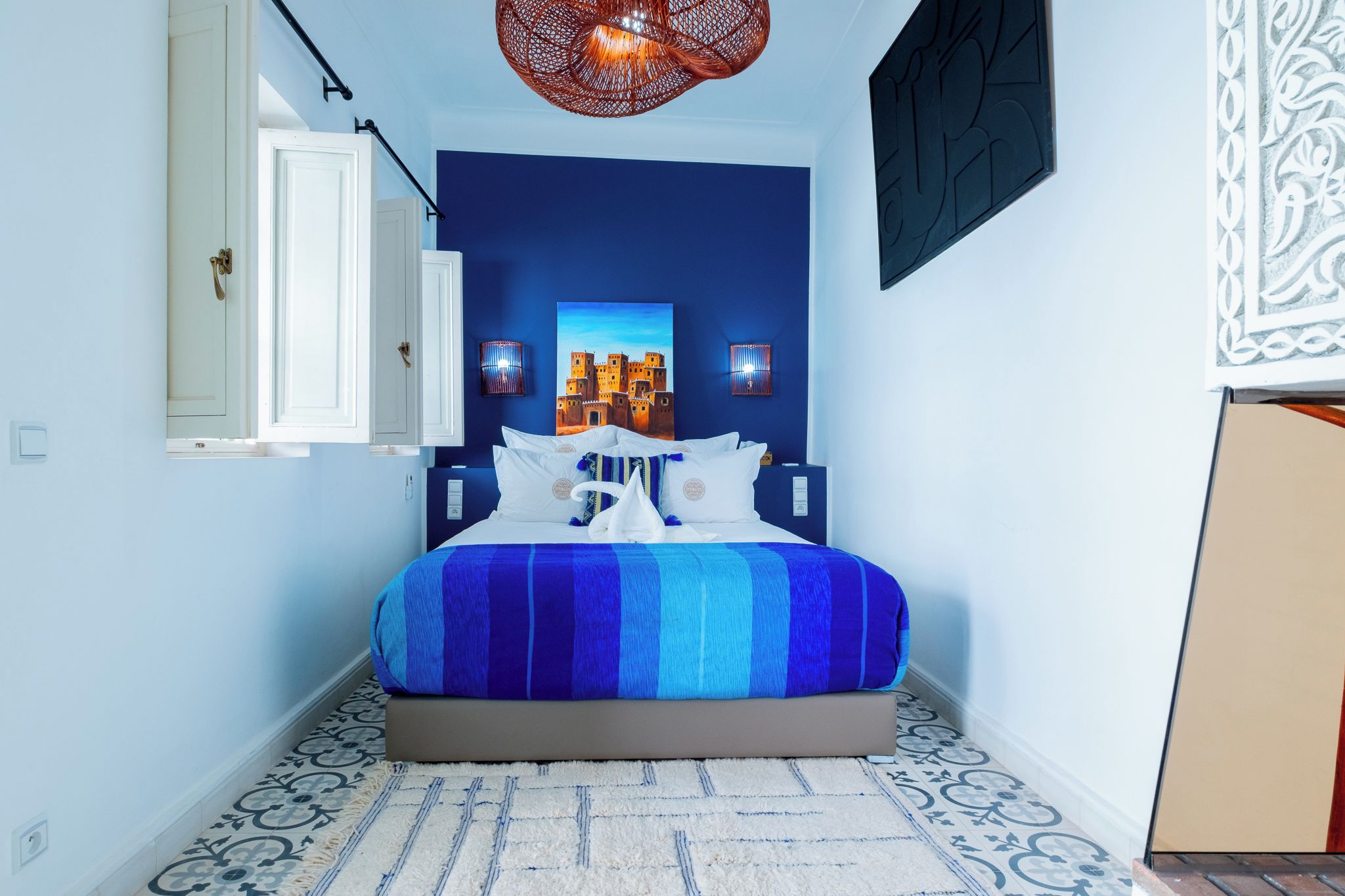 A bedroom with a bed, two wall-mounted lamps, a door, and a patterned floor.