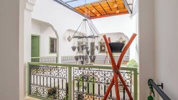 Un balcone con ringhiera in metallo, soffitto in legno e vista su un cortile con un lampadario.