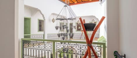 A balcony with a metal railing, a wooden ceiling, and a view of a courtyard with a hanging light fixture.