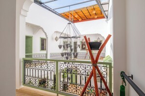 A balcony with a metal railing, a wooden ceiling, and a view of a courtyard with a hanging light fixture. - Riad Thaïs (Marrakech)
