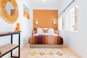 A bedroom with a bed, a round mirror, a painting, and a patterned rug. - Riad Thaïs (Marrakech)