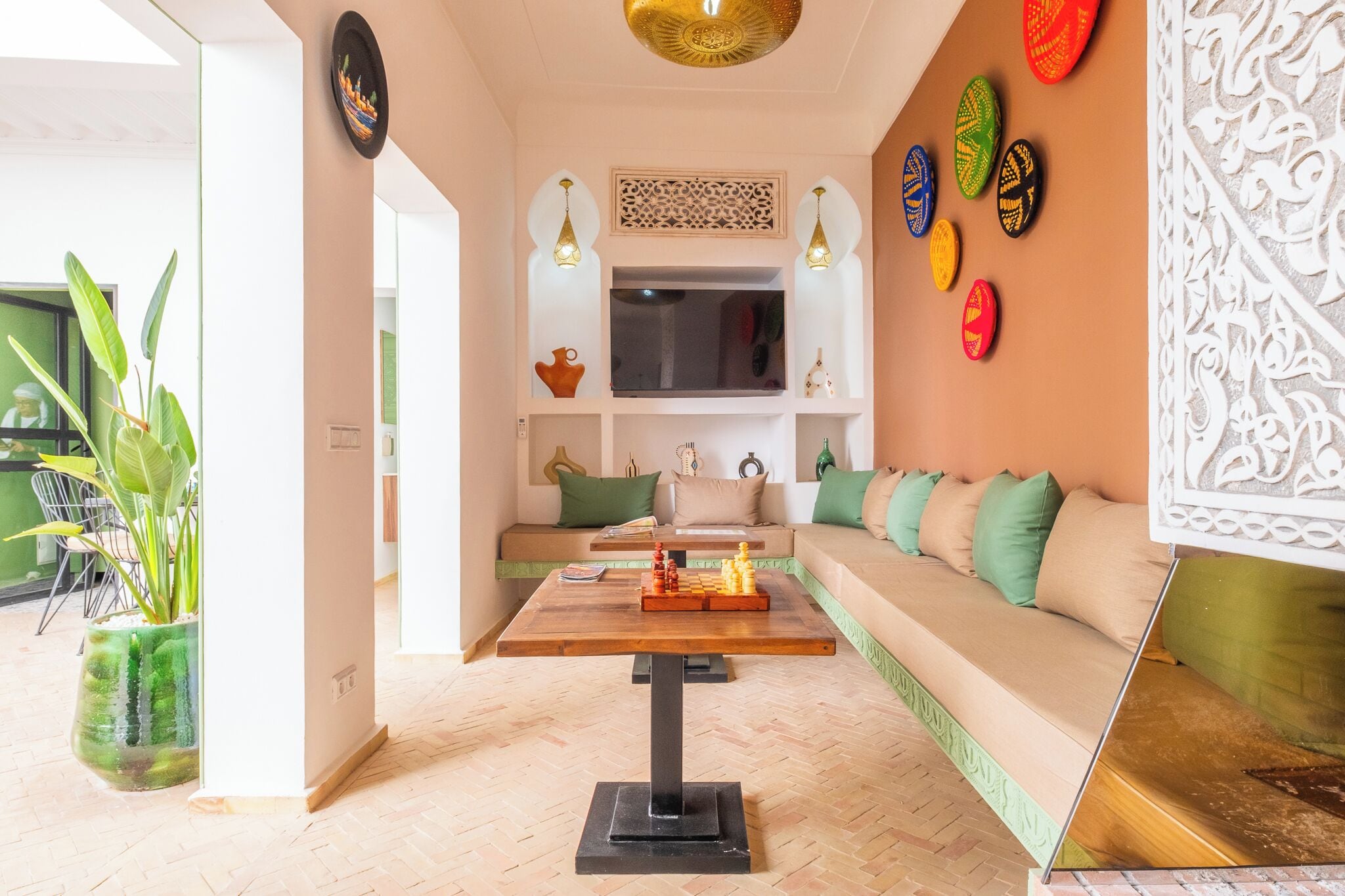 Ein modernes Wohnzimmer mit einer Couch, einem Couchtisch und einem Fernseher. An den Wänden hängen dekorative Teller und eine Pflanze steht in einem Topf.