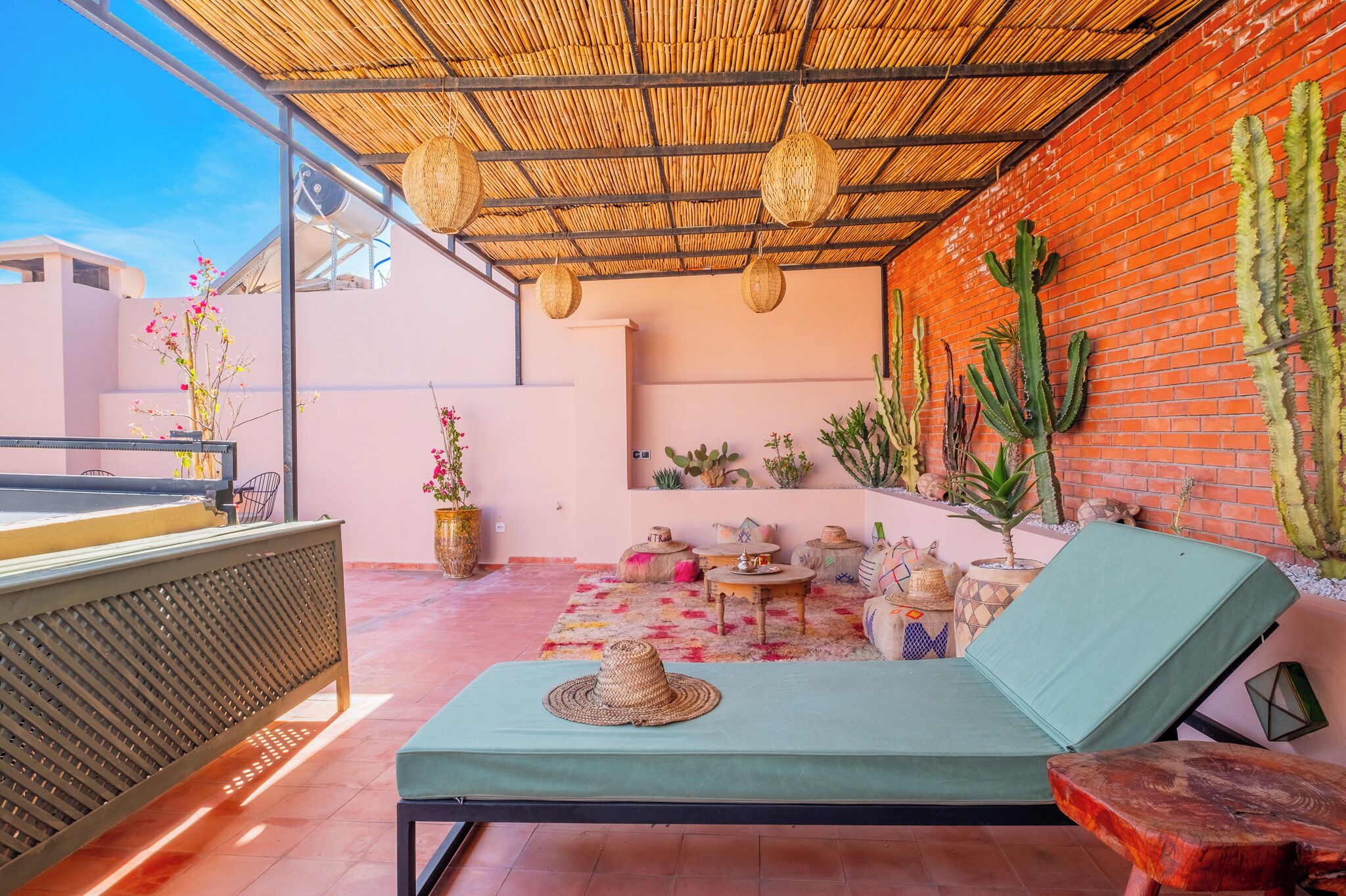 A rooftop lounge with a green cushioned seating area, a metal railing, and a variety of potted plants including cacti.