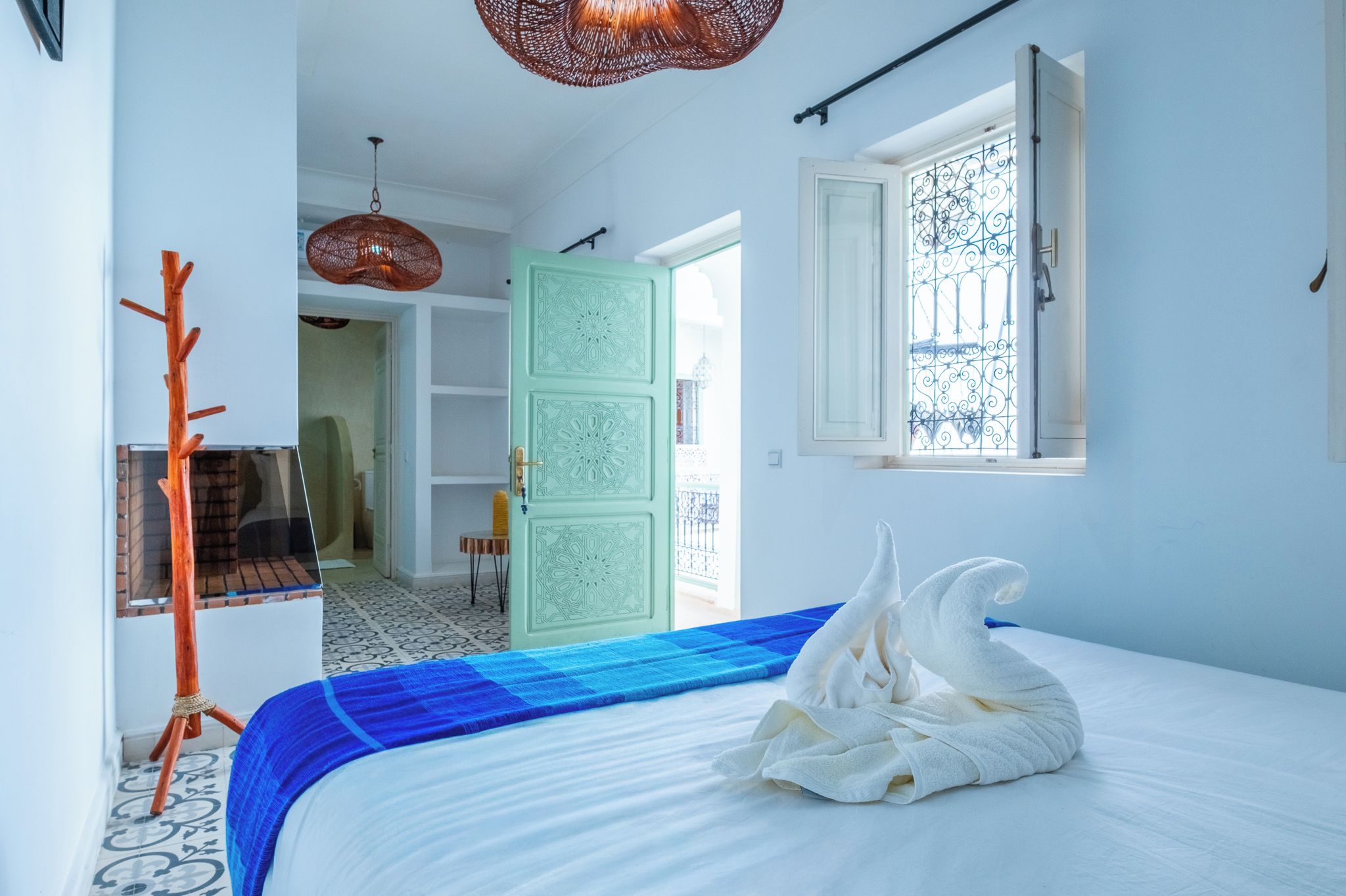 A bedroom with a bed, a wooden coat rack, a door with intricate patterns, and a window with decorative iron bars.