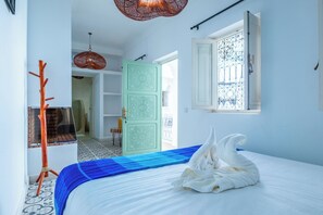 Un dormitorio con una cama, un perchero de madera, una puerta con diseños intrincados y una ventana con rejas decorativas de hierro.