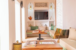 A cozy living room with a sofa, a coffee table, and a TV. - Riad Thaïs (Marrakech)