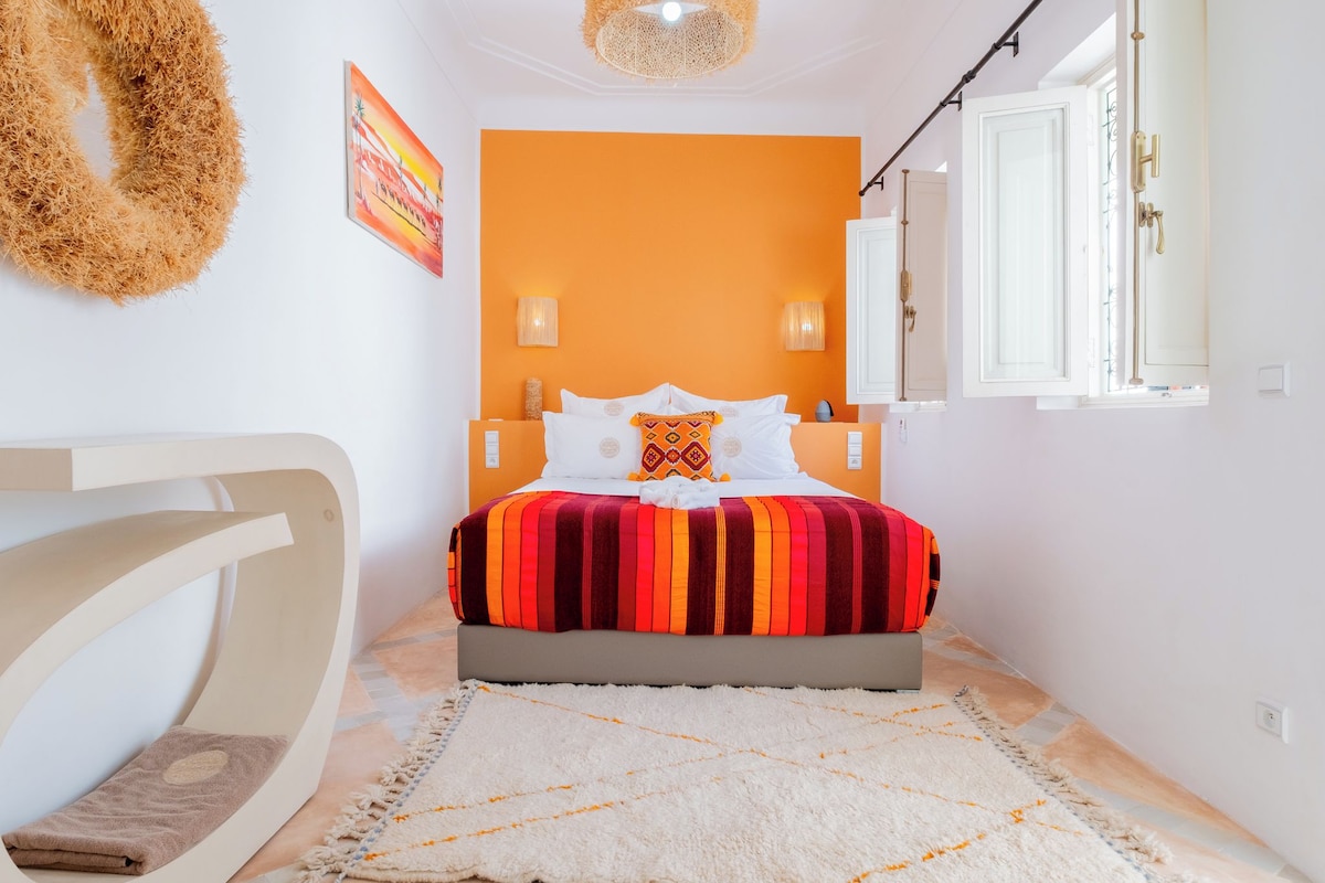 A bedroom with a bed, a white chair, a rug, and a wall with a painting.