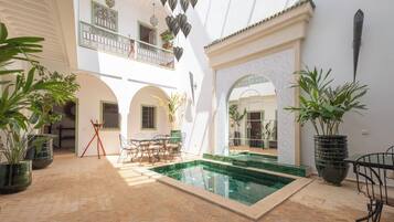 A spacious courtyard with a swimming pool, outdoor seating, and potted plants.