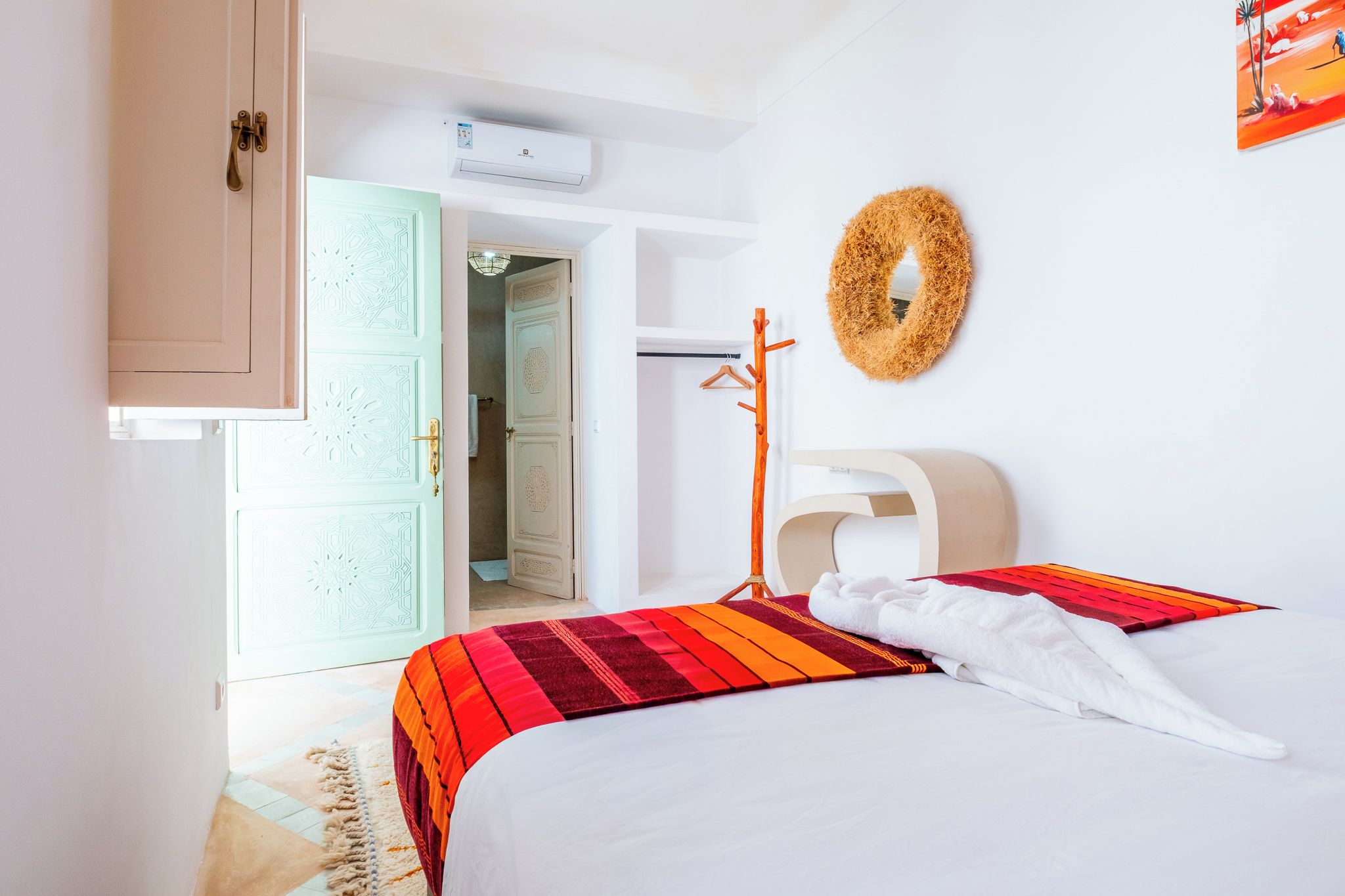 A hotel room with a bed, a headboard, a wall-mounted towel rack, and a door leading to a bathroom.