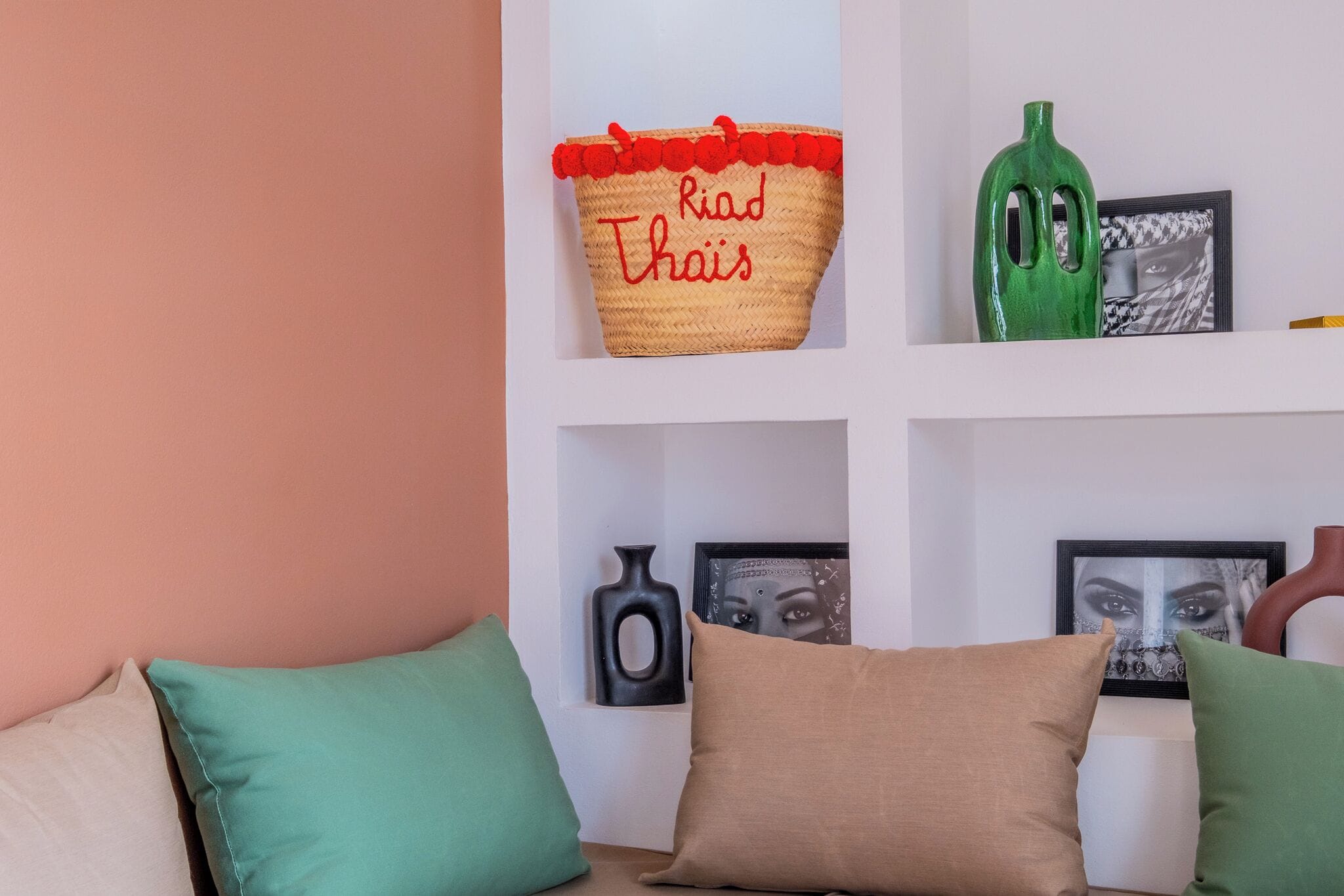 Ein Wohnzimmer mit einer Couch, Kissen, einem gewebten Korb mit Schriftzug, einer grünen Vase und gerahmten Bildern an der Wand.