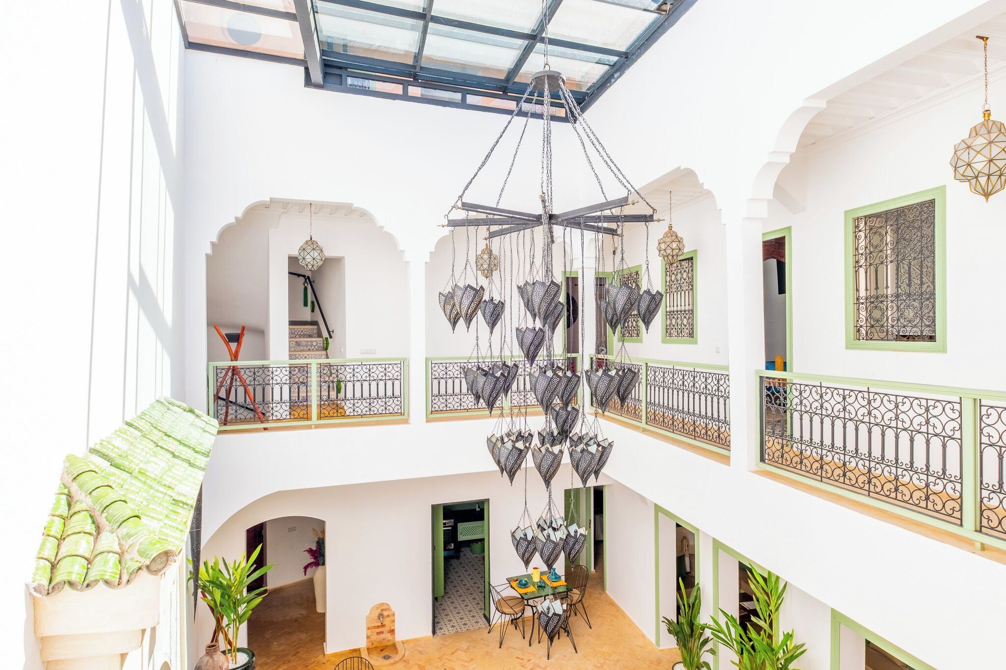 A multi-level interior with a central chandelier, balconies with wrought iron railings, and a dining area with chairs and a table.