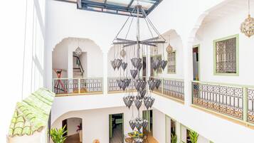 A multi-level interior with a central chandelier, balconies with wrought iron railings, and a dining area with chairs and a table.