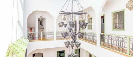 A multi-level interior with a central chandelier, balconies with wrought iron railings, and a dining area with chairs and a table.