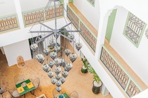A multi-level interior with a central hanging light fixture, a staircase, and patterned wall decorations. - Riad Thaïs (Marrakech)