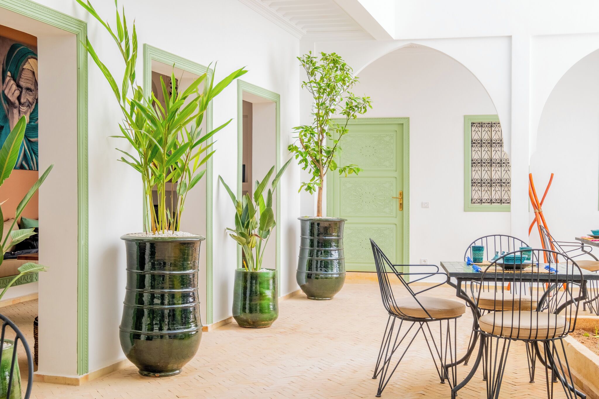 Un coin repas avec une table et des chaises, des plantes en pot et une porte verte.