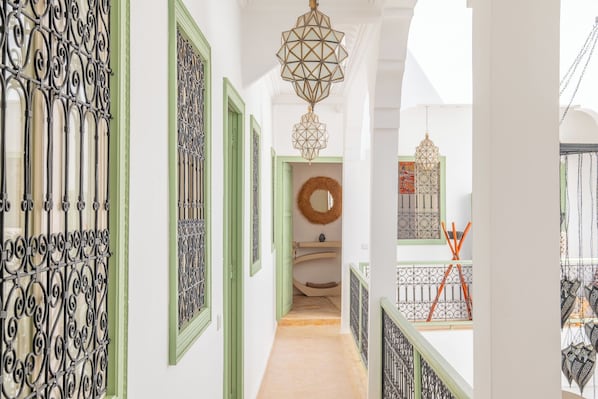 A corridor with ornate metal railings, a hanging light fixture, and a staircase with a patterned railing. - Riad Thaïs (Marrakech)