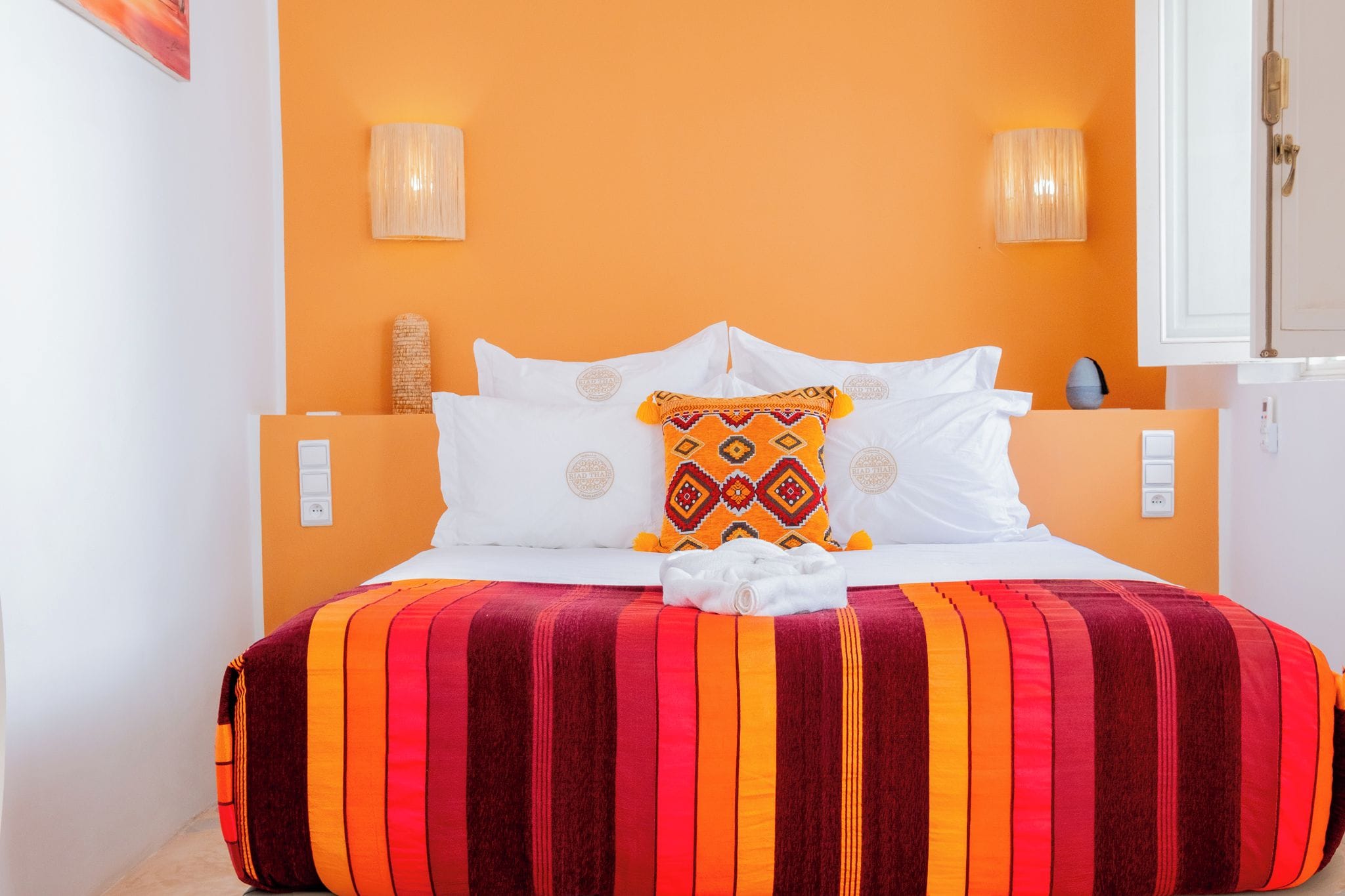 A hotel room with a bed, two wall-mounted lamps, and a textured wall.