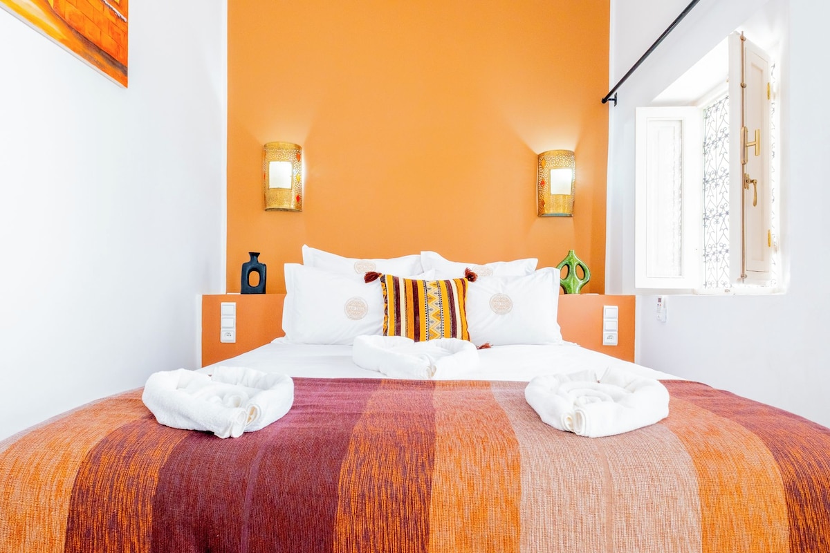 A hotel room with a bed, two wall-mounted lamps, a window with a curtain, and a towel on the bed.