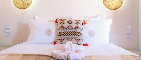 A hotel room with a bed, two decorative wall sconces, and a patterned throw pillow.