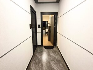 Ein schmaler Flur mit einer Tür am Ende, die zu einem Raum mit Kühlschrank und Mikrowelle führt.