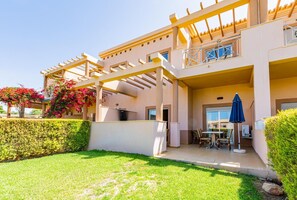 Un bâtiment à deux étages doté d’un patio couvert, d’un balcon et d’un petit espace extérieur aménagé avec une table et des chaises.