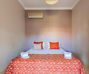 A hotel room with a bed, two pillows, a blanket, and a wall-mounted air conditioner. - 4-Bedroom Villa near the Beach – Casa Colina 2 (Albufeira)