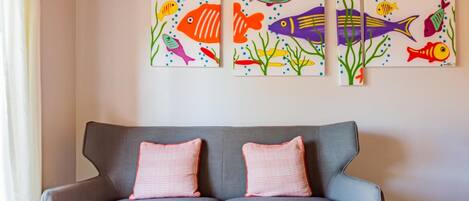 A grey sofa with two checkered cushions against a wall with three colorful fish paintings.