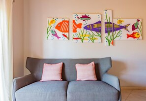 Ein graues Sofa mit zwei karierten Kissen vor einer Wand mit drei farbenfrohen Fischgemälden.