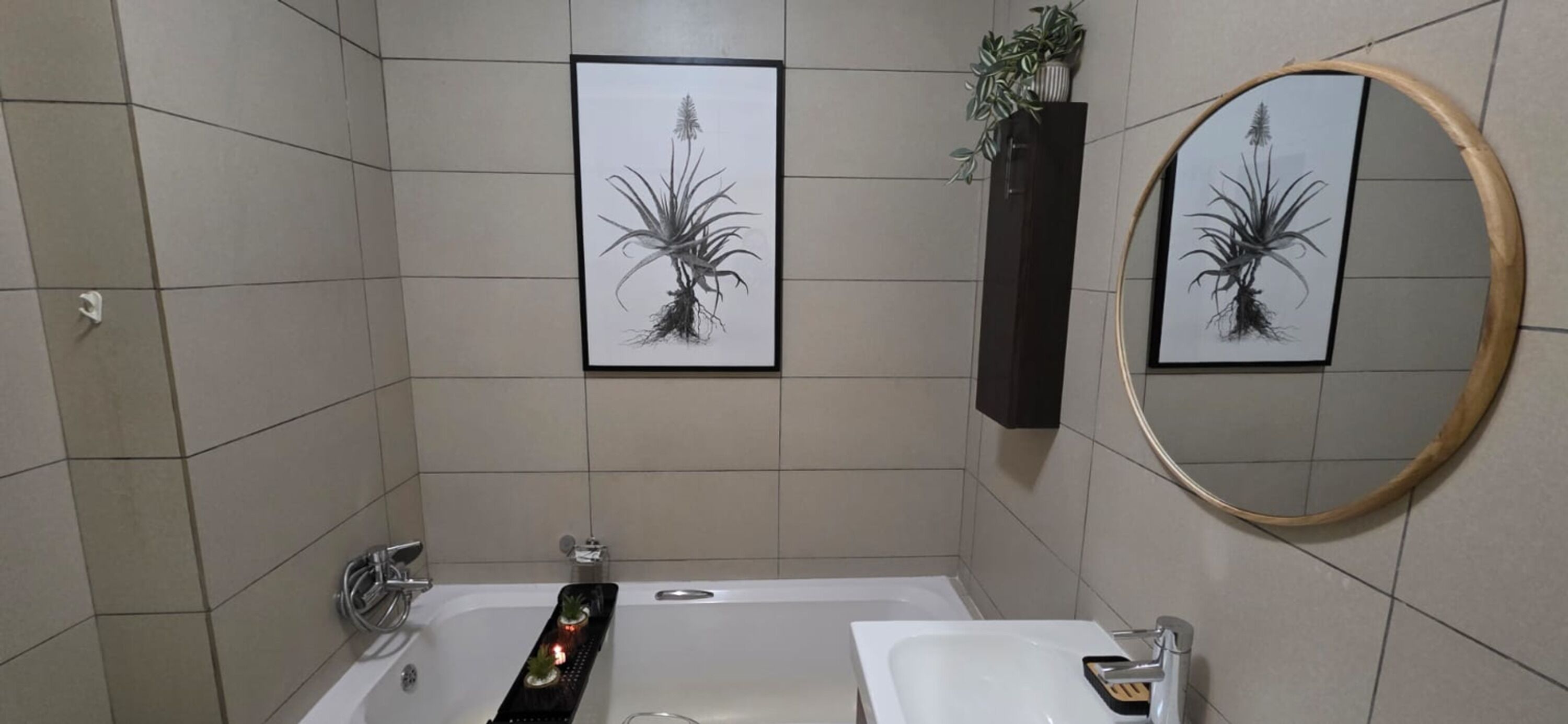 A bathroom with a bathtub, a sink, a mirror, and two framed pictures on the wall.