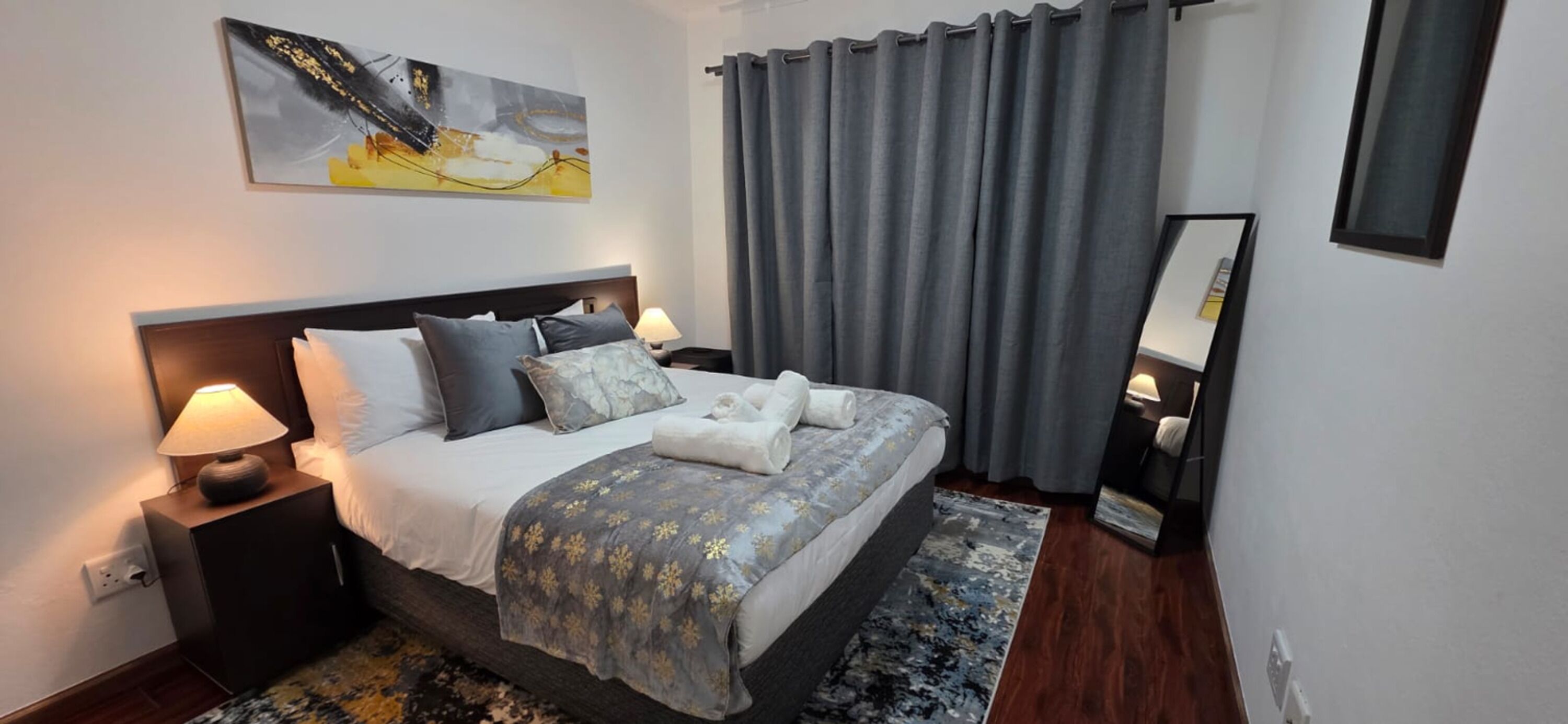 Ein Hotelzimmer mit einem Bett, Nachttischlampen, einem Teppich, einem Gemälde an der Wand und einem Fenster mit Vorhängen.