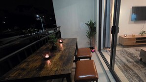 Un comedor con una mesa de madera, dos sillas y velas. Hay una planta en maceta y un televisor montado en la pared.