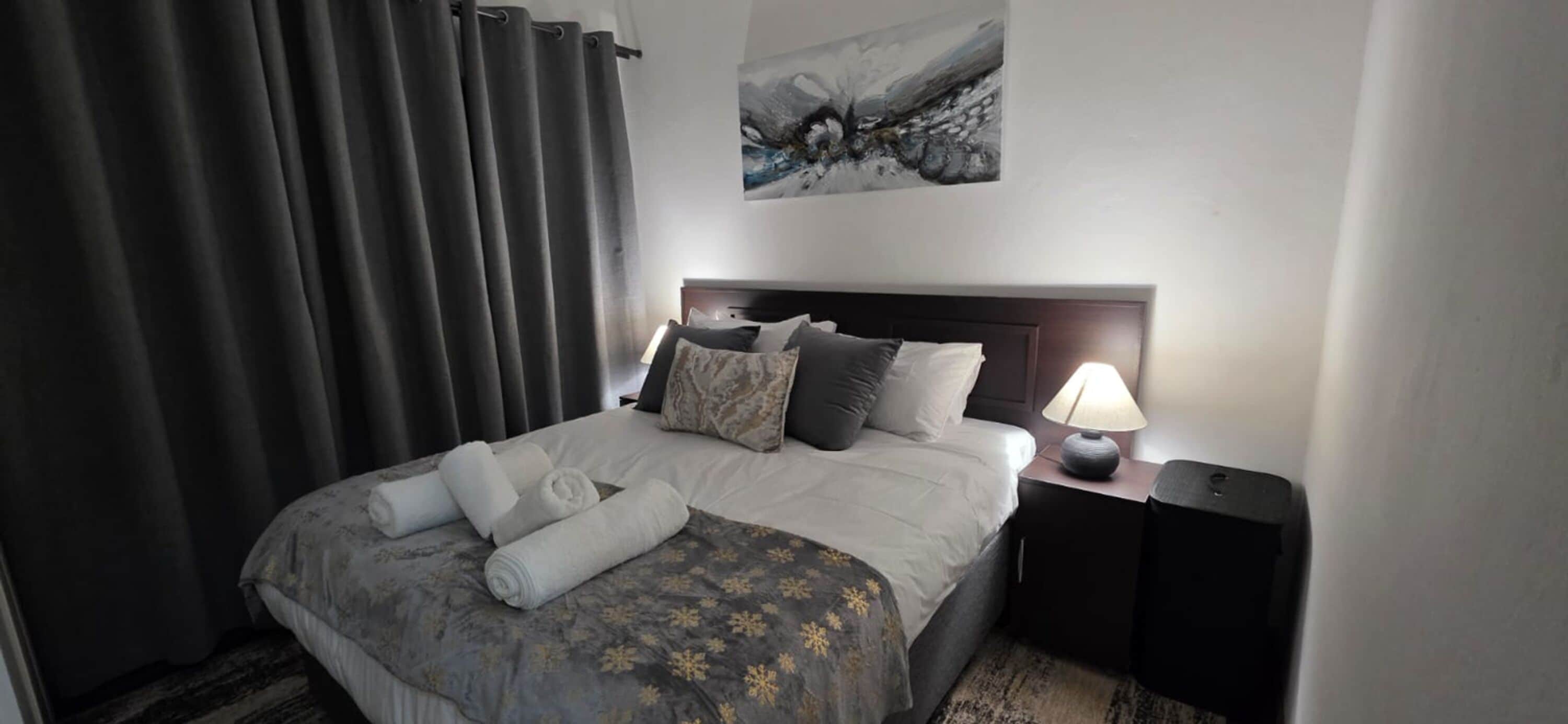 A hotel room with a bed, a nightstand, a lamp, and a painting on the wall.