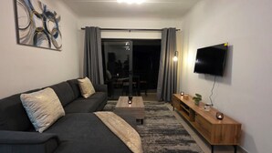 Una sala de estar moderna con un sofá, una mesa de centro, televisión y una mesita auxiliar de madera con adornos.