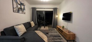 Ein modernes Wohnzimmer mit einer Couch, einem Couchtisch, einem Fernseher und einem Holztisch mit dekorativen Gegenständen.