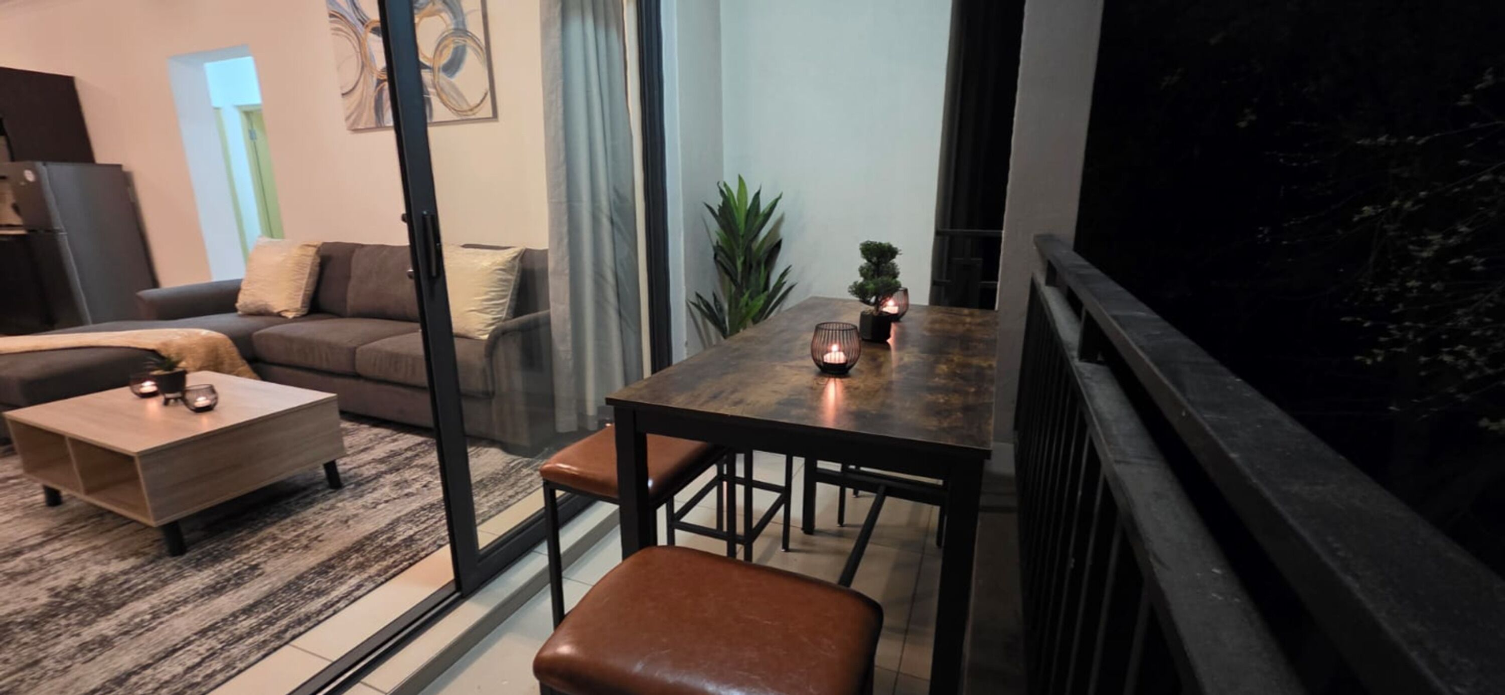 Een moderne woonkamer met een bank, salontafel en een eettafel met kaarsen.