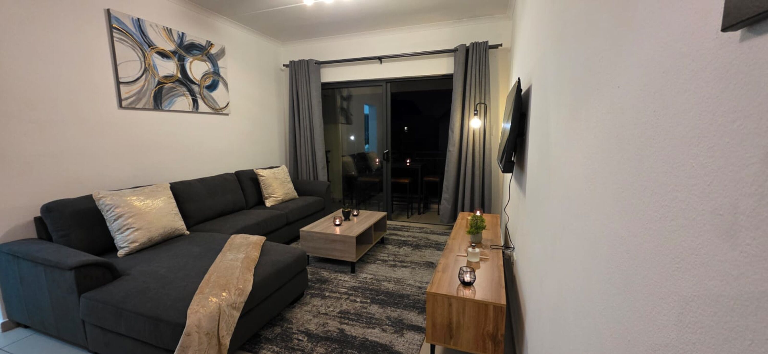A modern living room with a sofa, coffee table, and a flat-screen TV mounted on the wall.