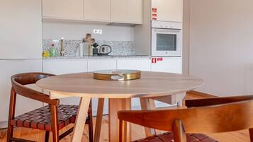 Una cocina compacta con gabinetes blancos, horno integrado y una mesa redonda de madera con sillas.