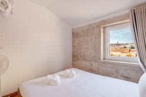 Quarto de hotel com uma cama, uma janela com vista para a paisagem urbana e uma parede de pedra.