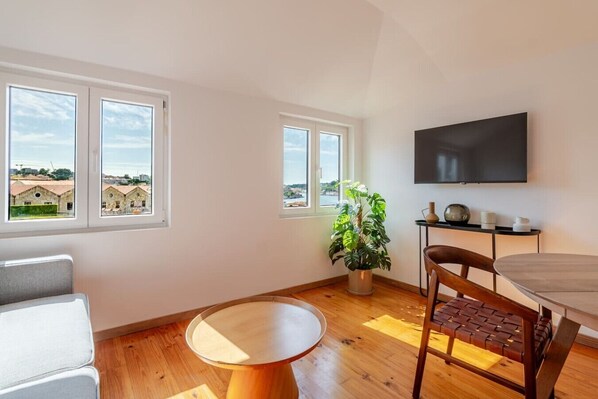 Een moderne woonkamer met een ronde houten tafel, een comfortabele bank, een kamerplant en een flatscreen televisie aan de muur.