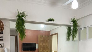 Una sala de estar con un sofá negro, una mesa de centro de vidrio y un televisor. Hay un armario de madera y un espejo en la pared.